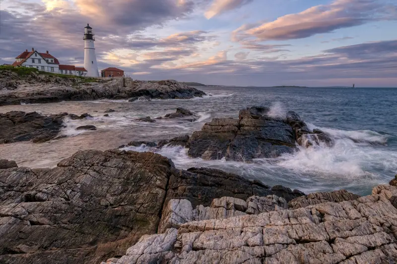 A white lighthouse above a rocky shoreline at dusk