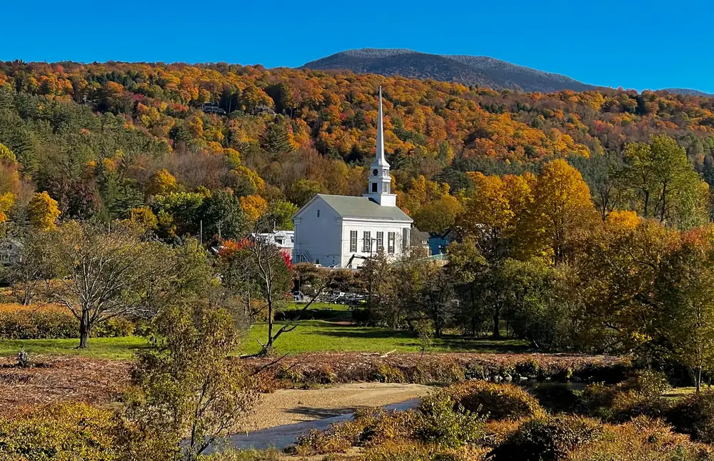 A white church steeple among autumn trees beneath a distant hillside